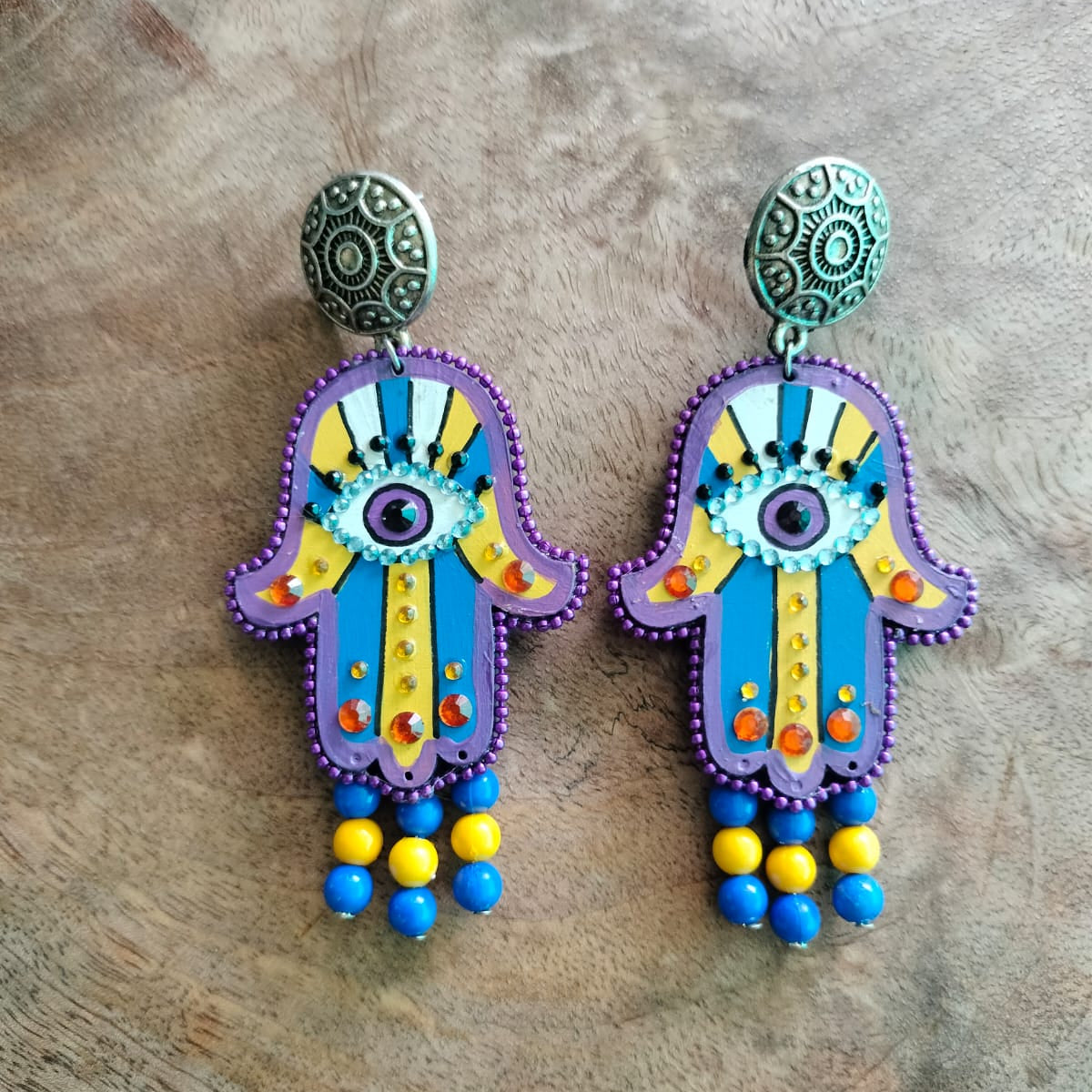 Colorful hamsa hand earrings on a wooden surface