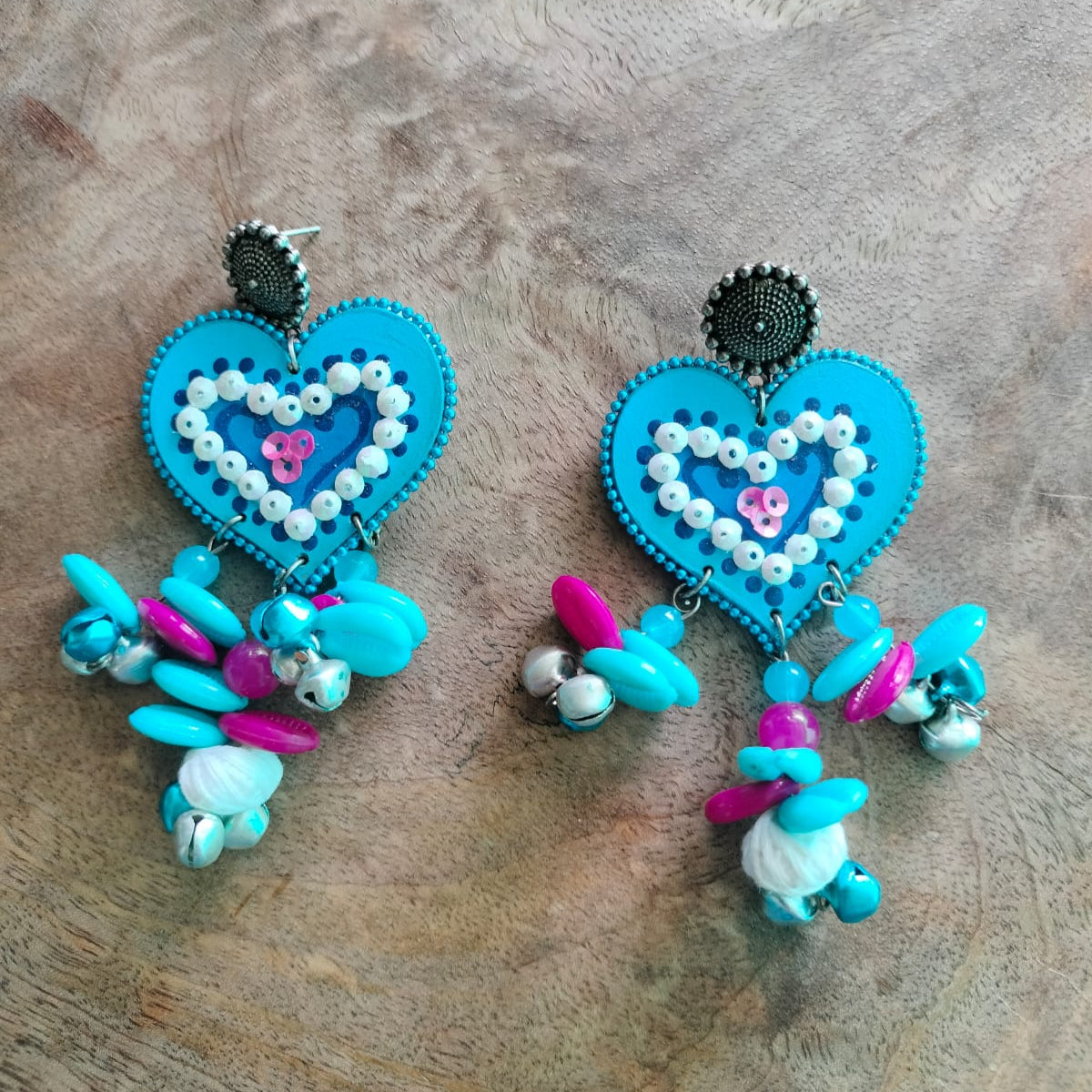 Pair of heart-shaped earrings with blue, pink, and white beads on a wooden surface
