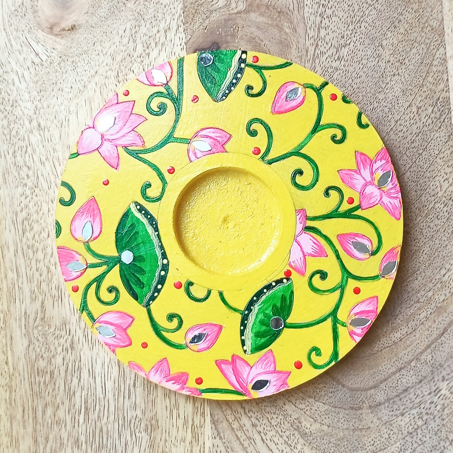 Decorative yellow plate with pink flowers and green leaves on a wooden surface