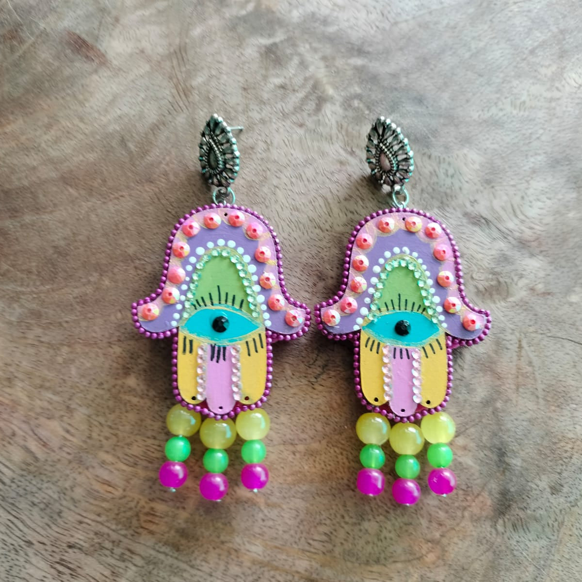 Colorful Hamsa hand earrings on a wooden surface
