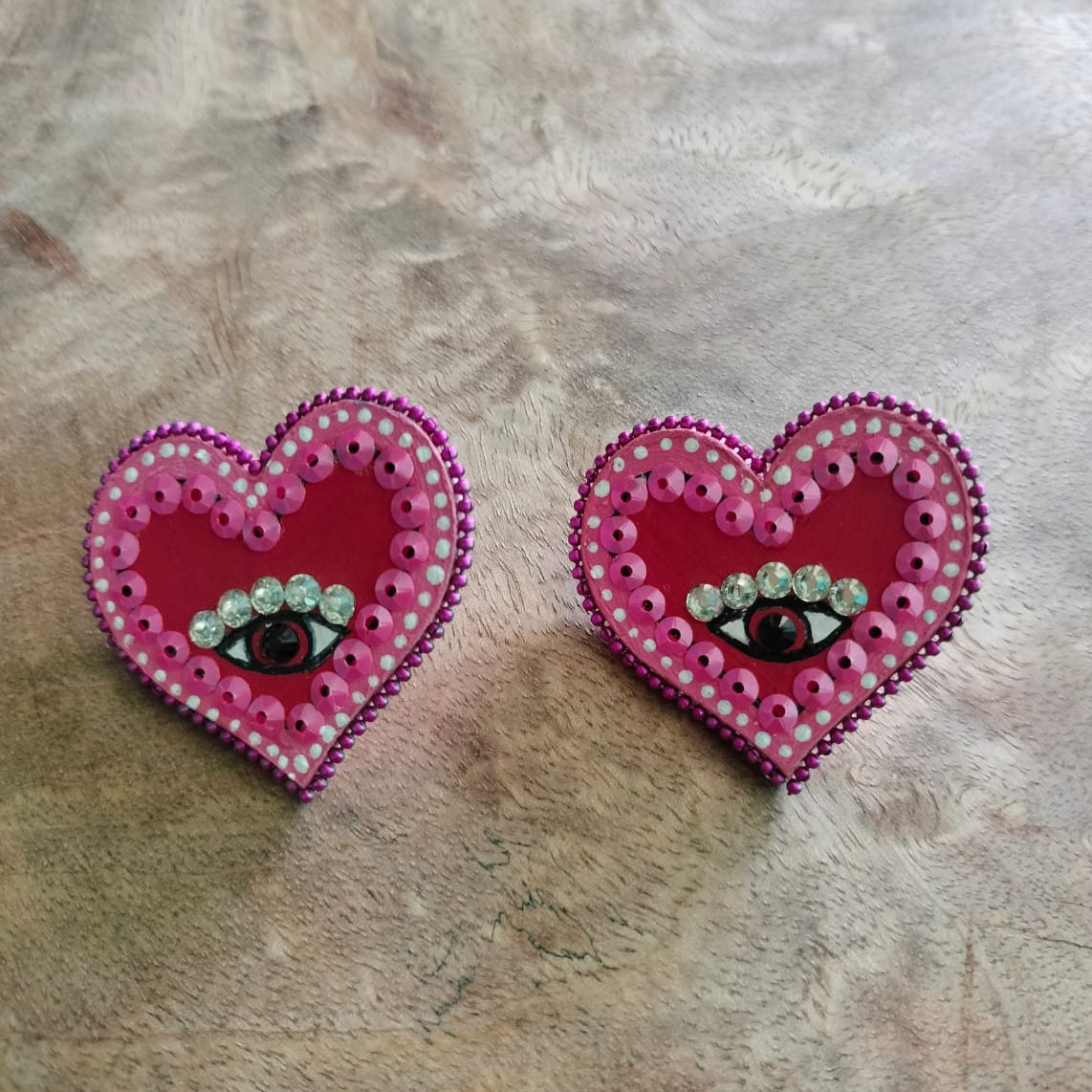Heart-shaped earrings with eye design on a wooden surface