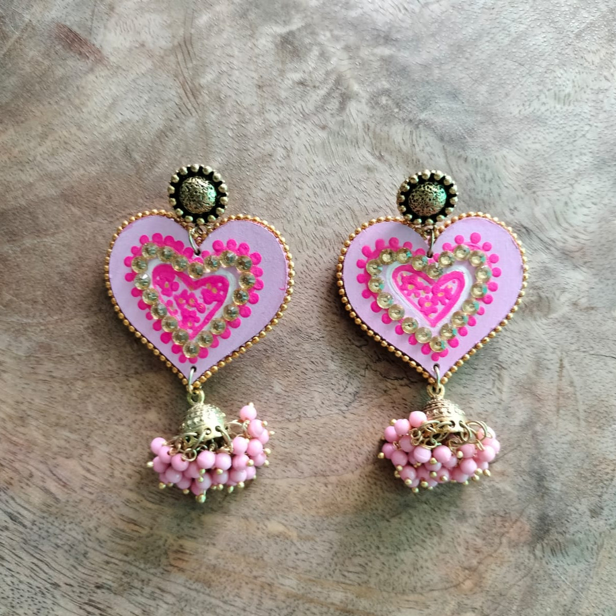 Heart-shaped earrings with pink and gold details on a wooden surface