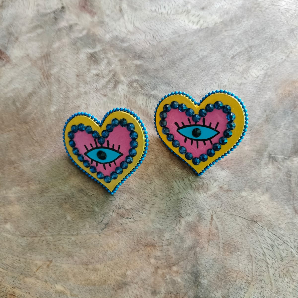 Heart-shaped earrings with eye design on a wooden textured surface